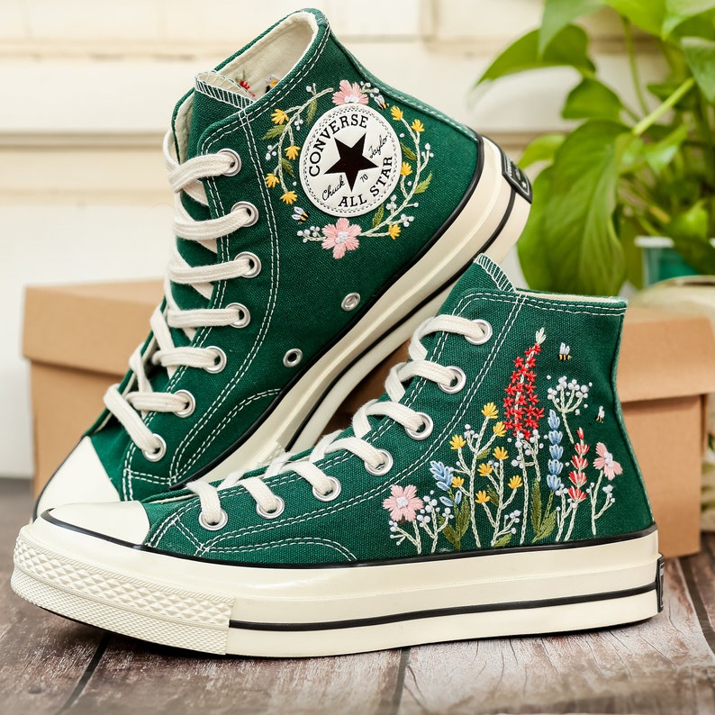 Może przedstawiać: Para zielonych, wysokich trampek Converse z haftowanymi wzorami kwiatowymi. Trampki mają białe podeszwy i sznur&oacute;wki. Lewa trampka ma logo Converse All Star z czarną gwiazdą.
