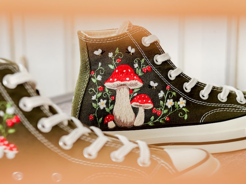 May include: A pair of green high-top canvas shoes with white laces and embroidered red and white mushrooms and flowers.