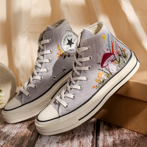 May include: Gray high-top Converse sneakers with white soles and colorful floral embroidery featuring mushrooms and other botanical elements.