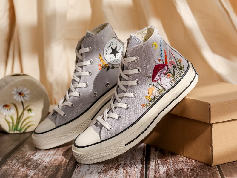 May include: Gray high-top Converse sneakers with white soles and colorful floral embroidery featuring mushrooms and other botanical elements.