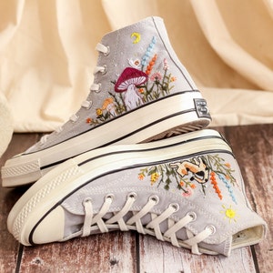 May include: A pair of gray canvas high-top sneakers with embroidered floral designs. One shoe features a mushroom and the other features a rabbit.