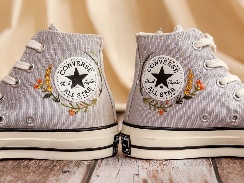 May include: A pair of gray high-top Converse sneakers with embroidered flowers and the text "Converse Chuck Taylor All Star" on the side.