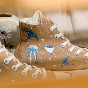 May include: A pair of beige canvas high-top sneakers with embroidered ocean-themed designs, including jellyfish, manta rays, and stars.