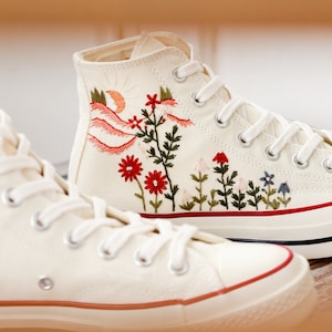 May include: A pair of white high-top canvas trainers with red, green and blue embroidered floral designs.