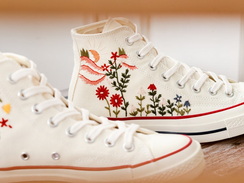 May include: A pair of white high-top canvas trainers with red, green and blue embroidered floral designs.