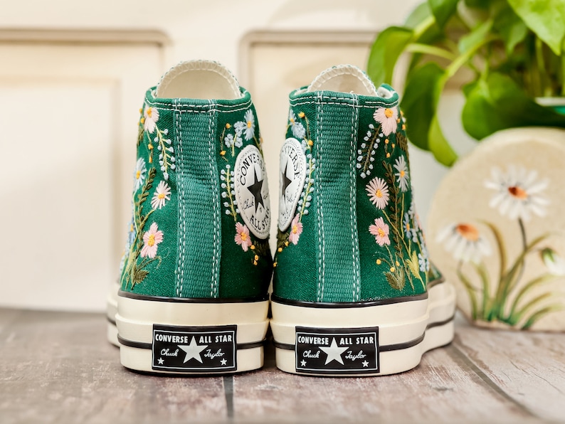 Puede incluir: Zapatillas altas de lona verde esmeralda, adornadas con dise&ntilde;os florales bordados en blanco, rosa y azul. Presentan el logo Converse All Star en el tobillo y suela blanca.