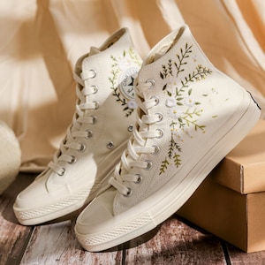 May include: A pair of off-white high-top canvas sneakers with floral embroidery. The sneakers have white laces and a white rubber sole.