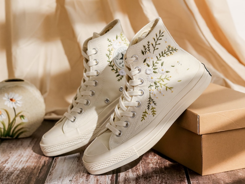 May include: A pair of off-white high-top canvas sneakers with floral embroidery. The sneakers have white laces and a white rubber sole.