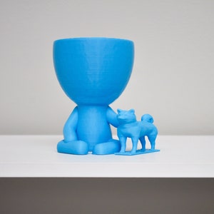 May include: A blue 3D printed planter shaped like a person holding a small blue 3D printed dog.