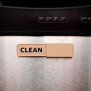 May include: A stainless steel washing machine with a beige "CLEAN" sign attached to the front.