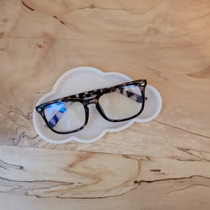 May include: A white cloud-shaped glasses holder with a pair of tortoise shell glasses resting on top.