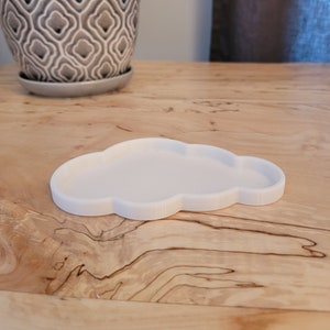 May include: A white cloud-shaped dish made of ceramic. The dish is sitting on a wooden surface.