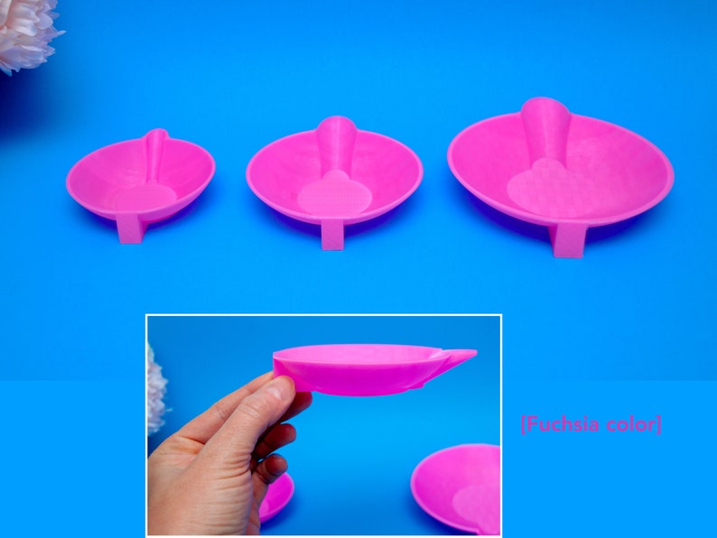 May include: Three fuchsia-colored, oval-shaped trays with attached spoon-like handles. The trays are arranged from smallest to largest, with a rectangular base supporting each. The background is a bright blue.