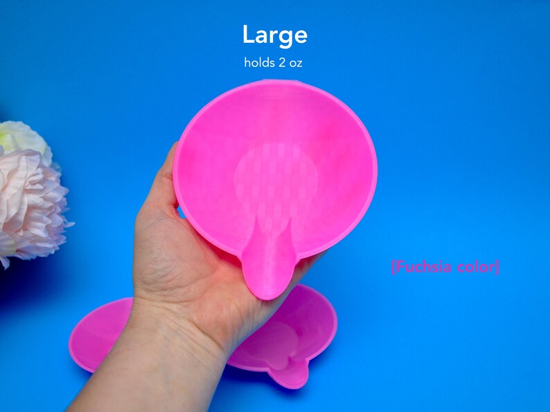 May include: A fuchsia-colored, large, round dish with a small handle. The dish holds 2 oz. The text "Large" and "holds 2 oz" are above the dish. The text "[Fuchsia color]" is below the dish. The dish is held by a hand against a blue background.