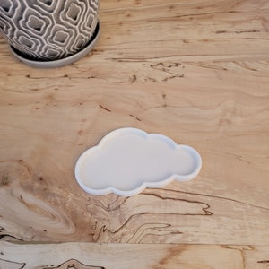 May include: White ceramic cloud-shaped dish on a wooden surface.