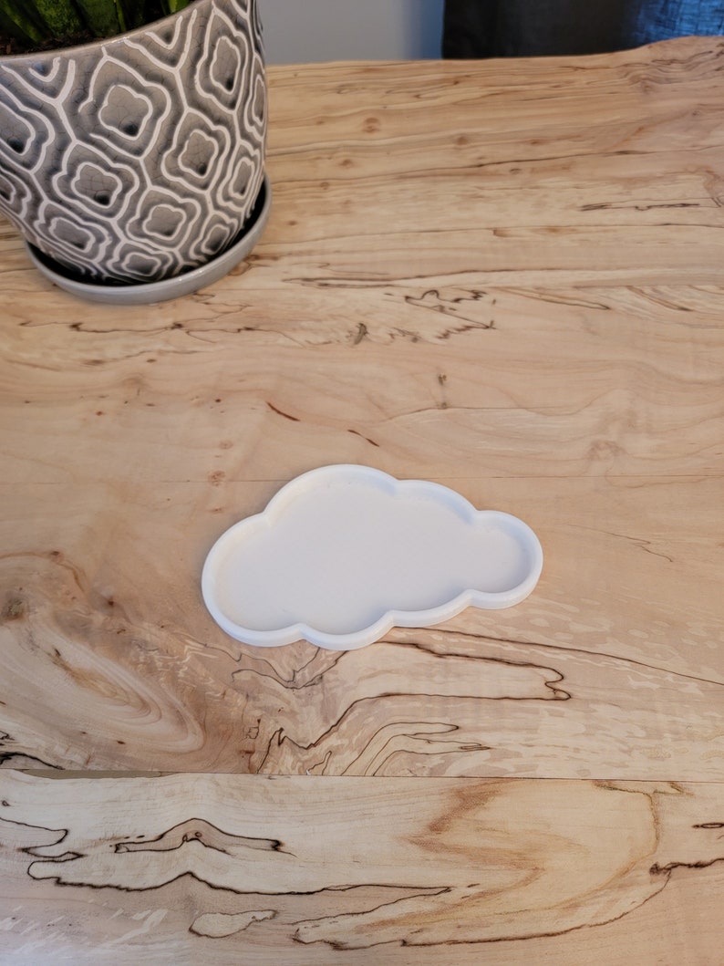 May include: White ceramic cloud-shaped dish on a wooden surface.