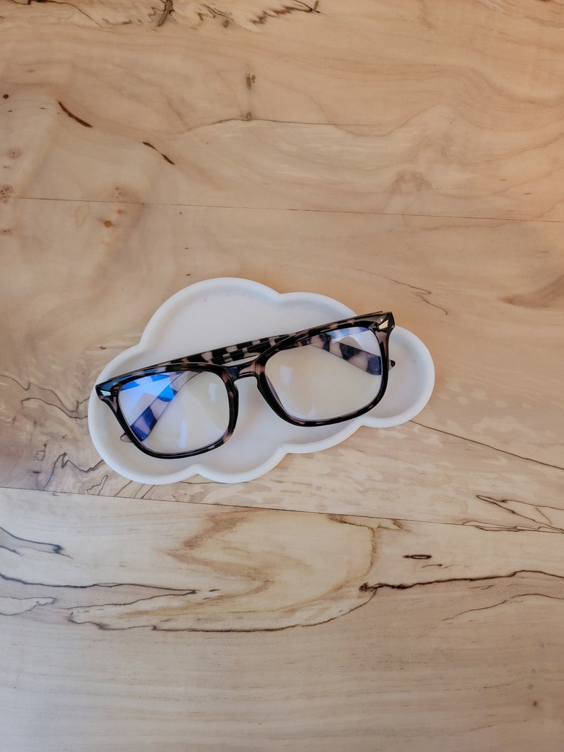 May include: A white cloud-shaped glasses holder with a pair of tortoise shell glasses resting on top.