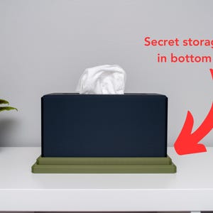 May include: A dark blue tissue box with a green base. The tissue box has a white tissue on top and the text "Secret storage in bottom" is written in red above the box.