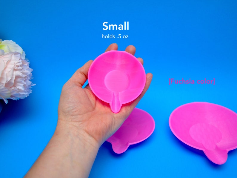 May include: Bright fuchsia-colored small dish with a unique shape, holding 0.5 oz. The dish is held in a hand against a vibrant blue background. The text "Small holds .5 oz" is visible.