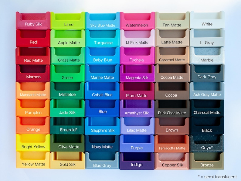 May include: A grid of colorful, small, plastic storage containers, each labeled with a different color name. Colors include Ruby Silk, Red, Red Matte, Maroon, Mandarin Matte, Pumpkin, Orange, Bright Yellow, Yellow Matte, Lime, Apple Matte, Grass Matte, Green, Mistletoe, Jade Silk, Emerald, Olive Matte, Gold Silk, Sky Blue Matte, Turquoise, Baby Blue, Marine Matte, Cobalt Blue, Blue, Sapphire Silk, Navy Matte, Blue Gray, Watermelon, Lt Pink Matte, Fuchsia, Magenta Silk, Plum Matte, Amethyst Silk, Lilac Matte, Purple, Indigo, Tan Matte, Latte Matte, Caramel Matte, Cocoa Matte, Cocoa, Dark Choc Matte, Brown, Terracotta Matte, Copper Silk, White, Lt Gray, Marble, Dark Gray, Ash Gray Matte, Charcoal Matte, Black, Onyx, Bronze.