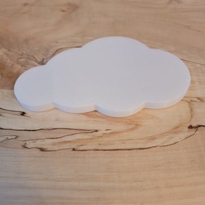 May include: A white cloud-shaped object made of a smooth, textured material. The object is sitting on a light brown wooden surface.
