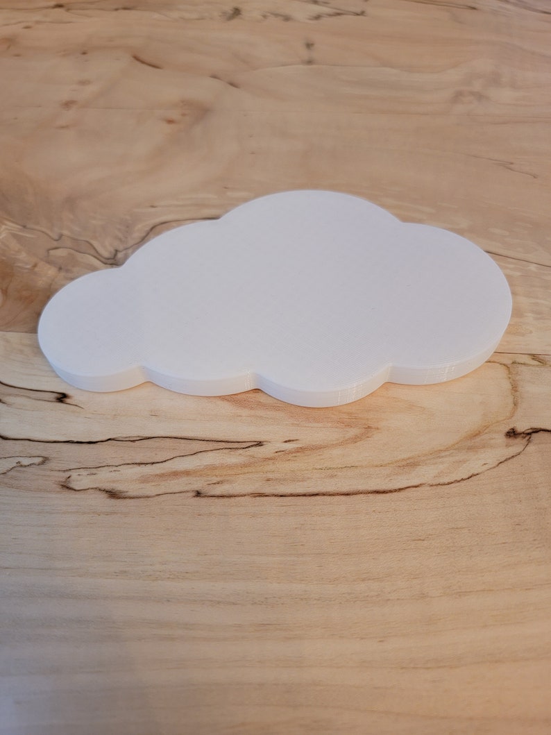 May include: A white cloud-shaped object made of a smooth, textured material. The object is sitting on a light brown wooden surface.