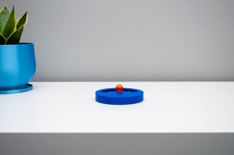 K&ouml;nnte beinhalten: Ein kreisf&ouml;rmiger blauer Kunststoffdeckel mit einem kleinen, mittig platzierten orangefarbenen Knaufgriff. Der Deckel hat eine flache, scheibenartige Form mit einem leicht erh&ouml;hten Rand und einer glatten Oberfl&auml;che f&uuml;r einen sicheren Verschluss.