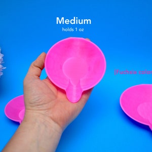 May include: Bright fuchsia-colored, medium-sized dish with a handle, holding 1 oz. The dish is shown against a vibrant blue background. The text "Medium holds 1 oz" and "[fuchsia color]" is visible.