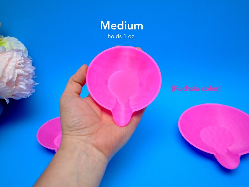 May include: Bright fuchsia-colored, medium-sized dish with a handle, holding 1 oz. The dish is shown against a vibrant blue background. The text "Medium holds 1 oz" and "[fuchsia color]" is visible.
