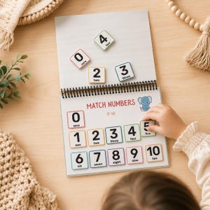 May include: A spiral-bound educational toy with number matching game. The game features numbered tiles from zero to ten, with corresponding word labels. The text "Match Numbers" is displayed on the cover. A child's hand is placing a tile.