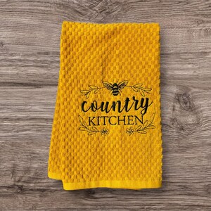 Pode incluir: Toalha de cozinha amarela com um design bordado preto que diz "country kitchen" com uma abelha e detalhes florais.