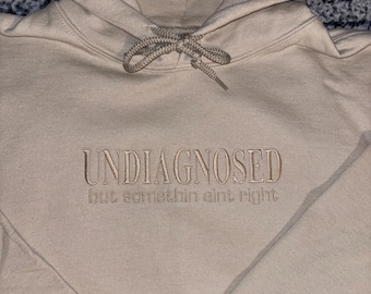 Funny Embroidered Sweatshirt – “Undiagnosed But Something Ain’t Right” | Sarcastic Quote Crewneck | Unisex Cozy Gift