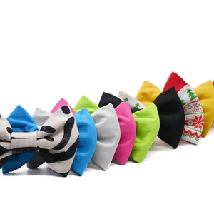 May include: A row of ten colorful bow ties, including a zebra print bow tie, a blue bow tie, a gray bow tie, a pink bow tie, a green bow tie, a black bow tie, a red and green patterned bow tie, a yellow bow tie, and a red bow tie.