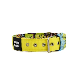 May include: A yellow dog collar with a colorful cartoon print and a silver buckle. The collar has the words "Double Trouble" printed on the side.