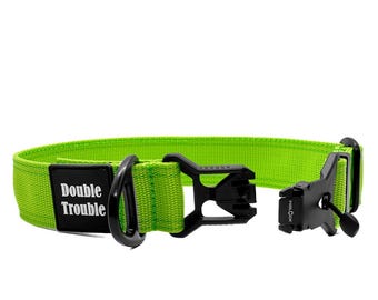 May include: Bright green dog collar with black hardware and the text "Double Trouble" on a black patch. The collar features a Fidlock buckle for secure fastening. A stylish accessory for pets.