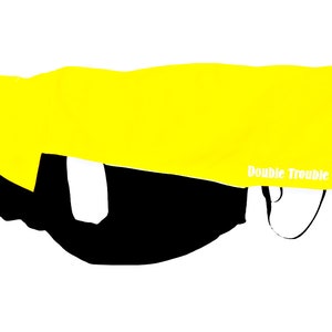 May include: A bright yellow dog coat with the text "Double Trouble" in white. The coat is partially covering a black object, and has straps. The background is white.