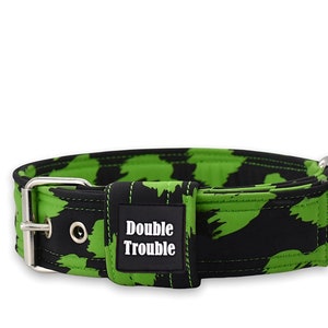 Puede incluir: Un collar de perro negro y verde con una hebilla plateada y un parche negro que dice "Double Trouble".