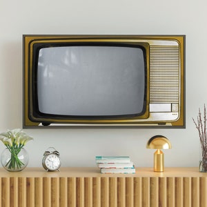 Puede incluir: Un televisor de estilo vintage con marco dorado y pantalla negra se encuentra sobre una estantería de madera con una lámpara dorada y un jarrón de flores blancas.