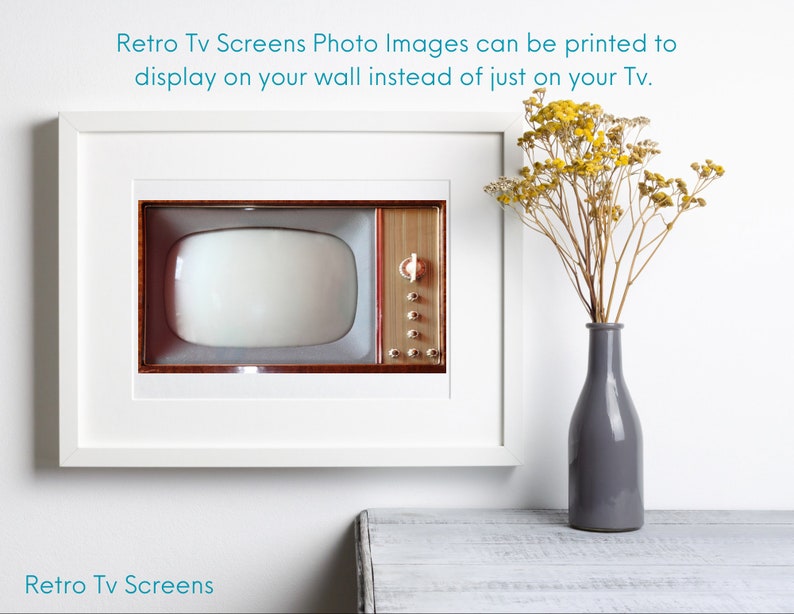May include: A white picture frame with a vintage television screen inside. The television is brown with a white screen. The frame is hanging on a white wall. A vase with dried yellow flowers is on a white table below the frame.