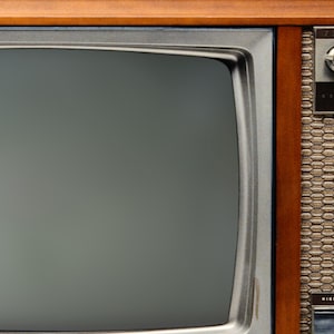 May include: A vintage Zenith television with a woodgrain cabinet and a black and white screen. The television has a silver metal bezel around the screen and a silver metal control panel on the right side. The control panel has a knob for tuning the channels and a knob for adjusting the volume.