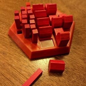May include: A red wooden puzzle game with a hexagonal base. The game features various red wooden blocks of different shapes and sizes, including rectangular and cube-shaped pieces. One piece is detached.