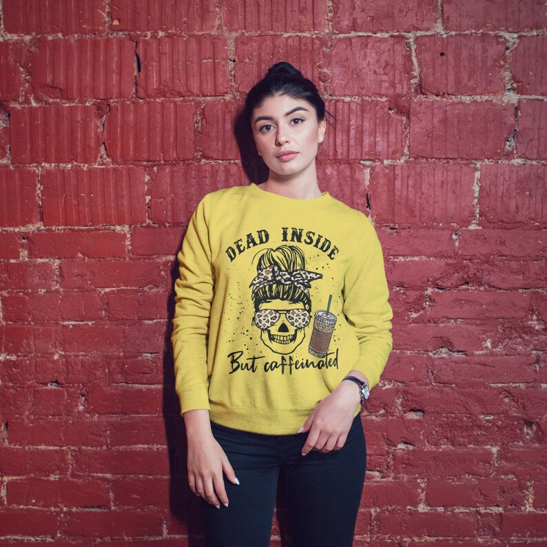 May include: Yellow sweatshirt with a skull graphic and the text "Dead inside but caffeinated". The skull is wearing sunglasses and a leopard print headband.