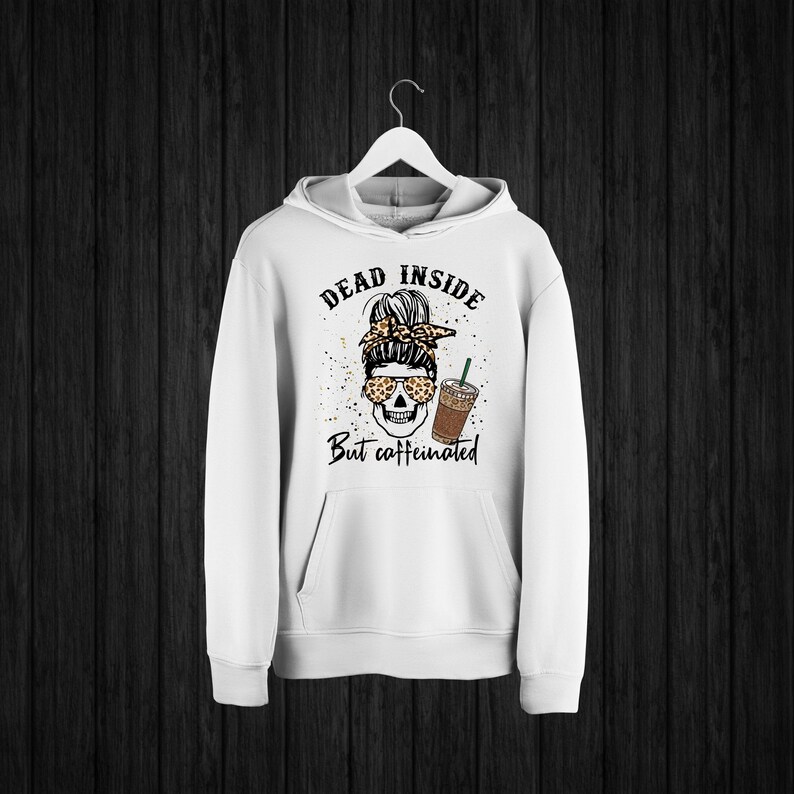 May include: White hoodie with a skull wearing sunglasses and a leopard print headband holding a cup of iced coffee. The text on the hoodie reads "Dead inside but caffeinated".