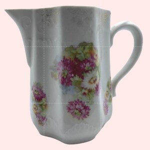 May include: White porcelain pitcher with a floral design featuring pink, white, and green flowers. The pitcher has a scalloped rim and handle, with gold accents. A decorative piece for serving beverages.