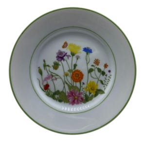 May include: White ceramic plate with a green rim and a floral design. The plate features a colorful illustration of wildflowers, including yellow, purple, orange, and pink blooms, with a small butterfly. The plate is round.