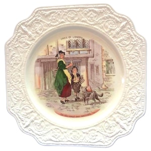 Puede incluir: Plato decorativo blanco con borde festoneado y diseño floral en relieve. El centro presenta una ilustración colorida de una mujer y un niño con un perro, con el texto "Cries of London" y "Do you want any matches?"