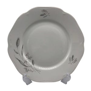 May include: White ceramic plate with a scalloped edge and a floral design in black. The plate has a central recessed area and is supported by a clear plastic stand. The floral design includes wheat and other plant elements.