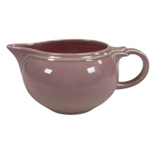 Puede incluir: Una cremera de cerámica de color malva con pico y asa. La cremera tiene un cuerpo redondeado y un acabado liso y brillante. El interior es de un tono malva más oscuro.