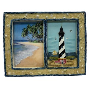 May include: A decorative double photo frame with a beach theme. The frame has a sandy texture with seashells and a blue rope border. One side features a beach scene with palm trees, and the other a lighthouse with black and white stripes.