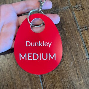 May include: Red oval-shaped keychain with a silver ring and clasp. The keychain has the text "Dunkley MEDIUM" printed in white.